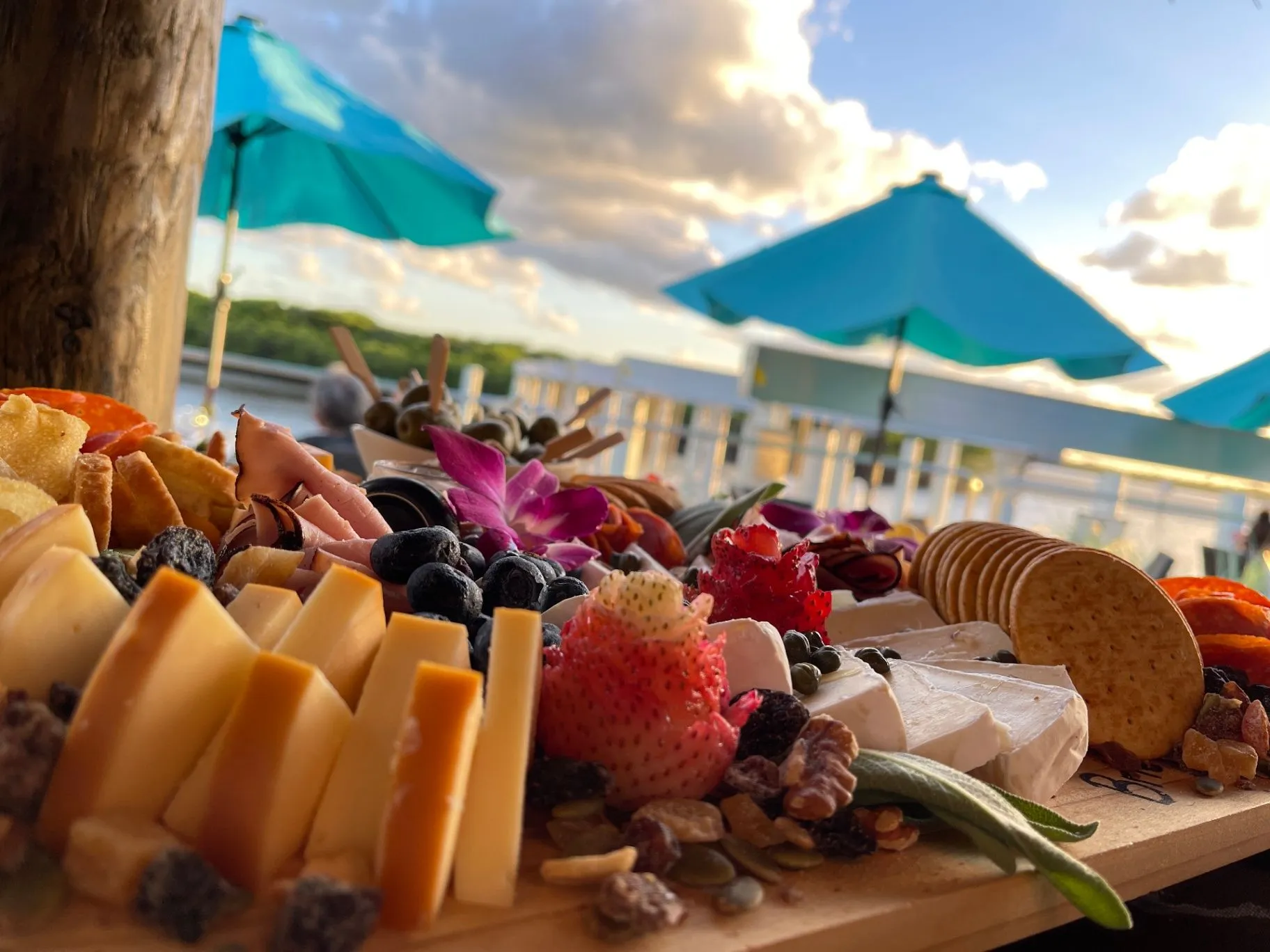 Close-up of a catering charcuterie board beside waterfront umbrellas