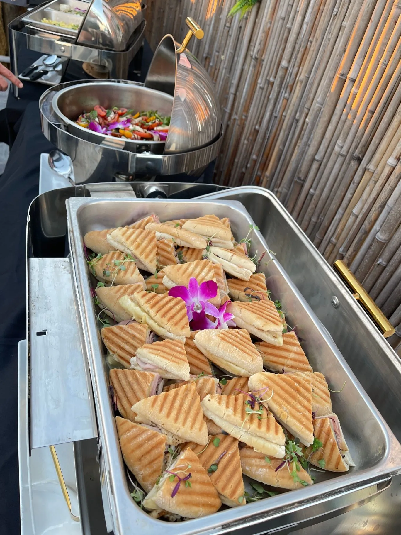 Catering buffet tray of grilled panini sandwiches beside chafing dishes